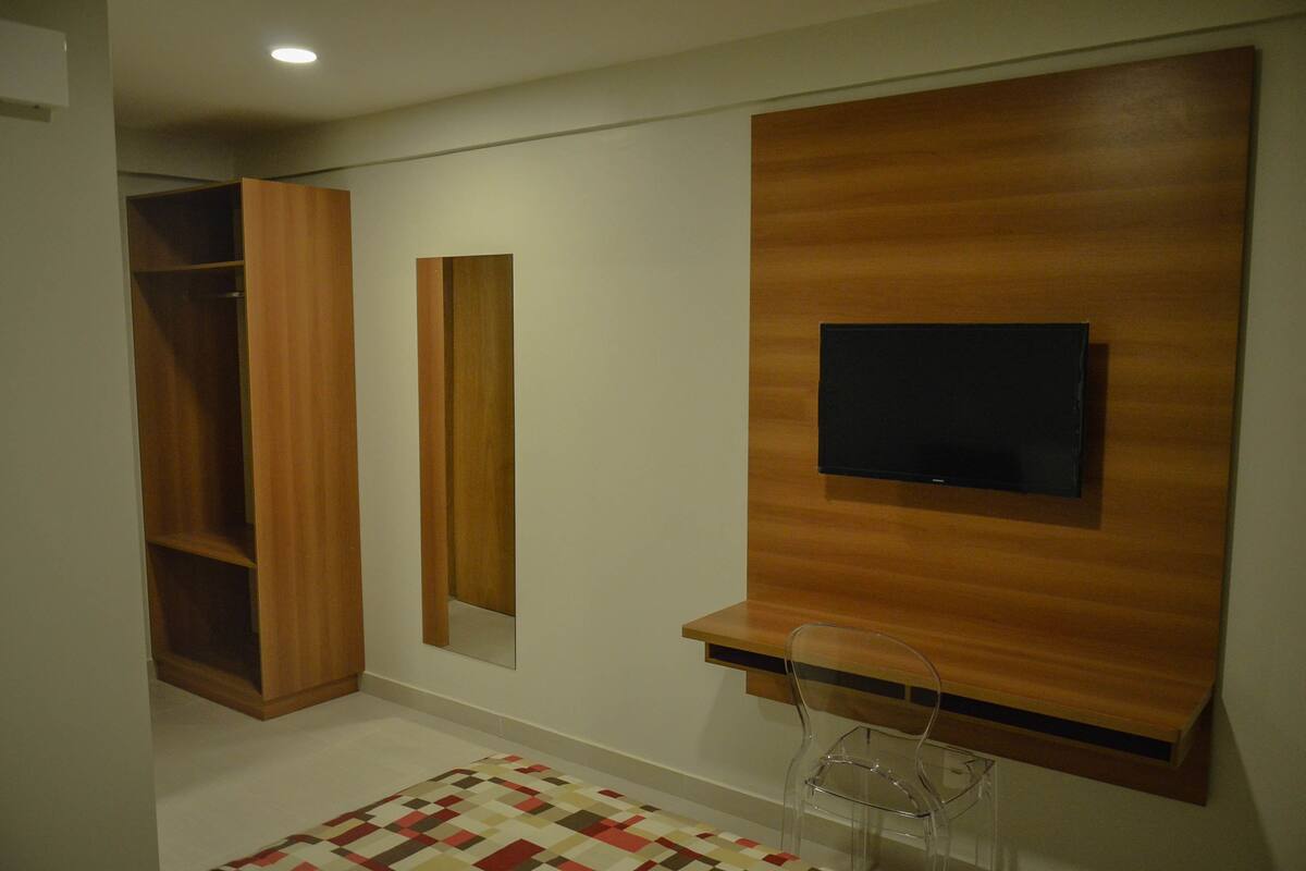 Una habitación moderna con un armario empotrado de madera, un televisor montado en la pared y una silla transparente.