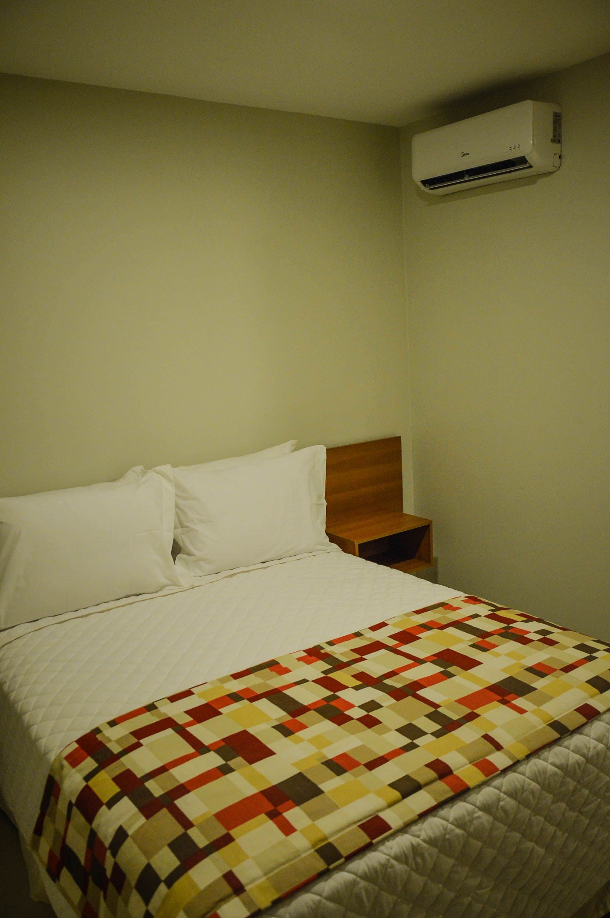Ein Bett mit einer Decke, ein Nachttisch und eine Wand-Klimaanlage.