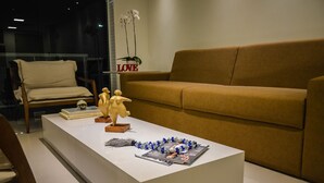 Una sala de estar moderna con un sofá color beige, una mesa de centro blanca que exhibe objetos decorativos y una silla de madera.