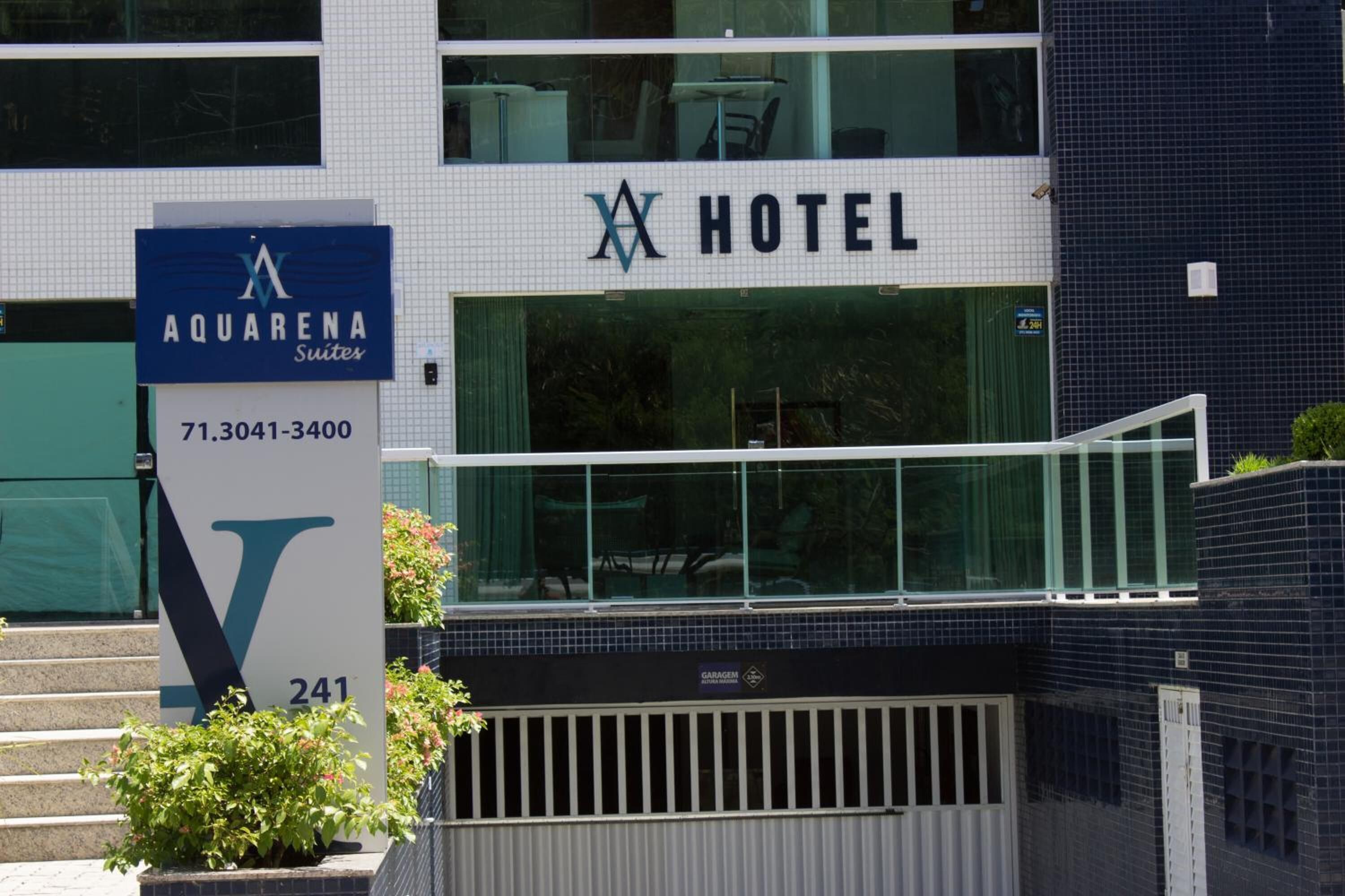 A hotel with a sign for Aquarena Suites, featuring a large 'V' logo and contact number.