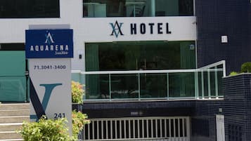 Um hotel com uma placa para Aquarena Suites, exibindo um grande logotipo em formato de 'V' e um número de contato.