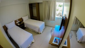 Une chambre d’hôtel avec deux lits simples, un bureau avec un ordinateur portable, un miroir et une fenêtre avec des rideaux.