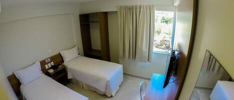 A hotel room with two single beds, a desk with a laptop, a mirror, and a window with curtains.