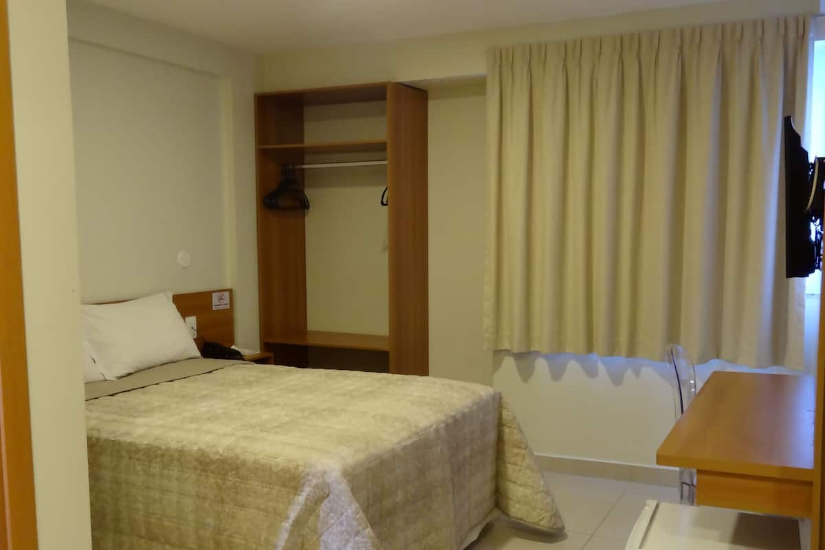 Una habitación de hotel con una cama, un armario, una mesita y un refrigerador.