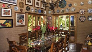 A dining area with a glass table, wooden chairs, and a variety of decorative plates on the walls. - Orchidelirium Casa Hotel & Salud Estetica (Cuernavaca)