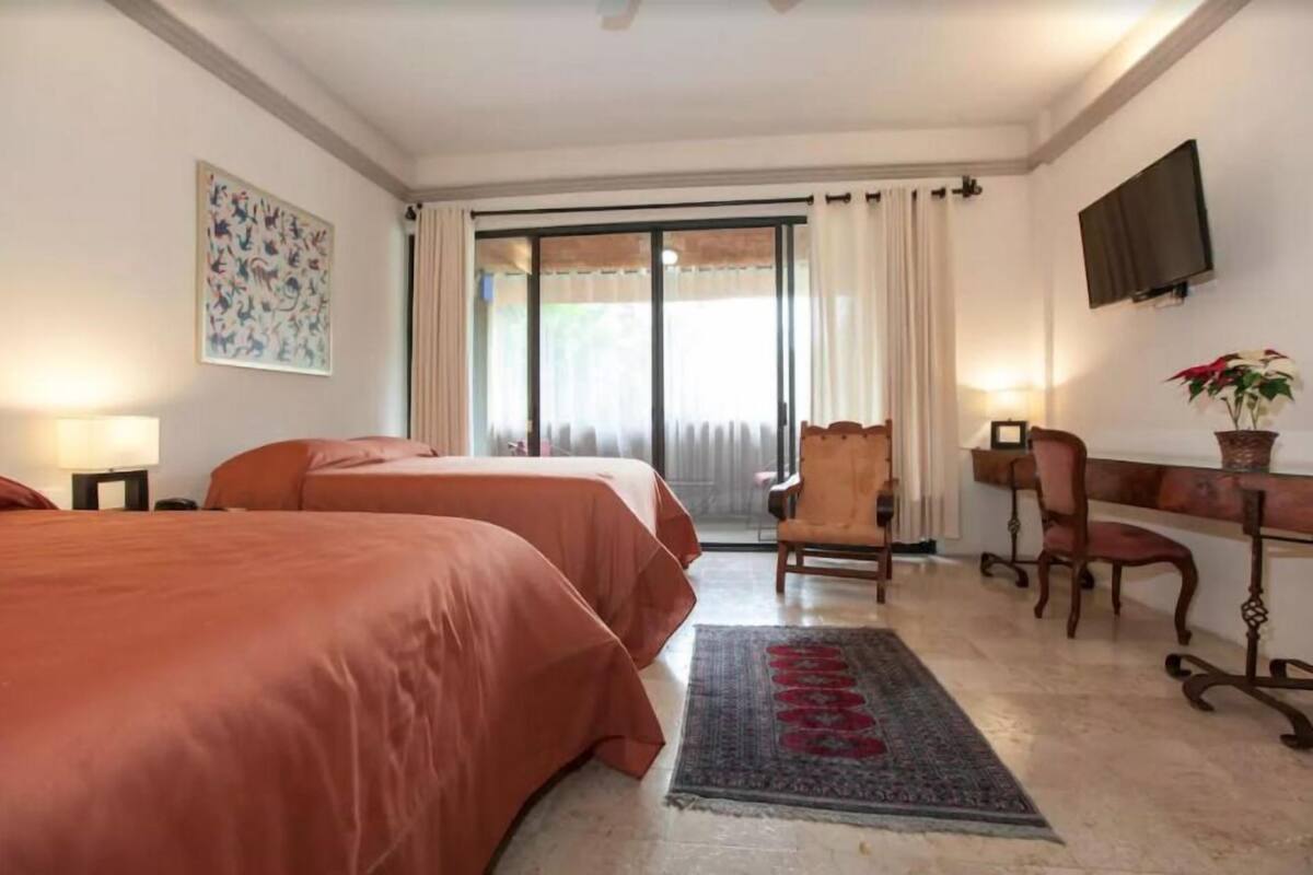 Une chambre d’hôtel avec deux lits, un bureau, une chaise, une télévision et une grande fenêtre avec des rideaux.