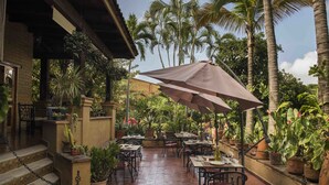 An outdoor patio with tables and chairs, surrounded by potted plants and palm trees. - Orchidelirium Casa Hotel & Salud Estetica (Cuernavaca)