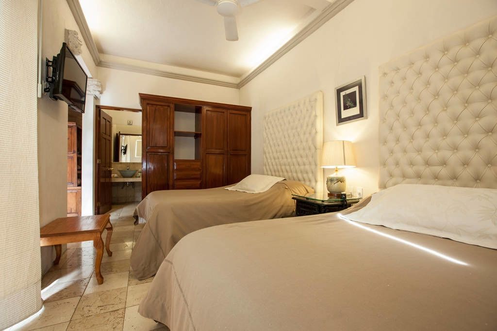 Habitación de hotel con dos camas, un armario de madera, un televisor y un ventilador de techo.