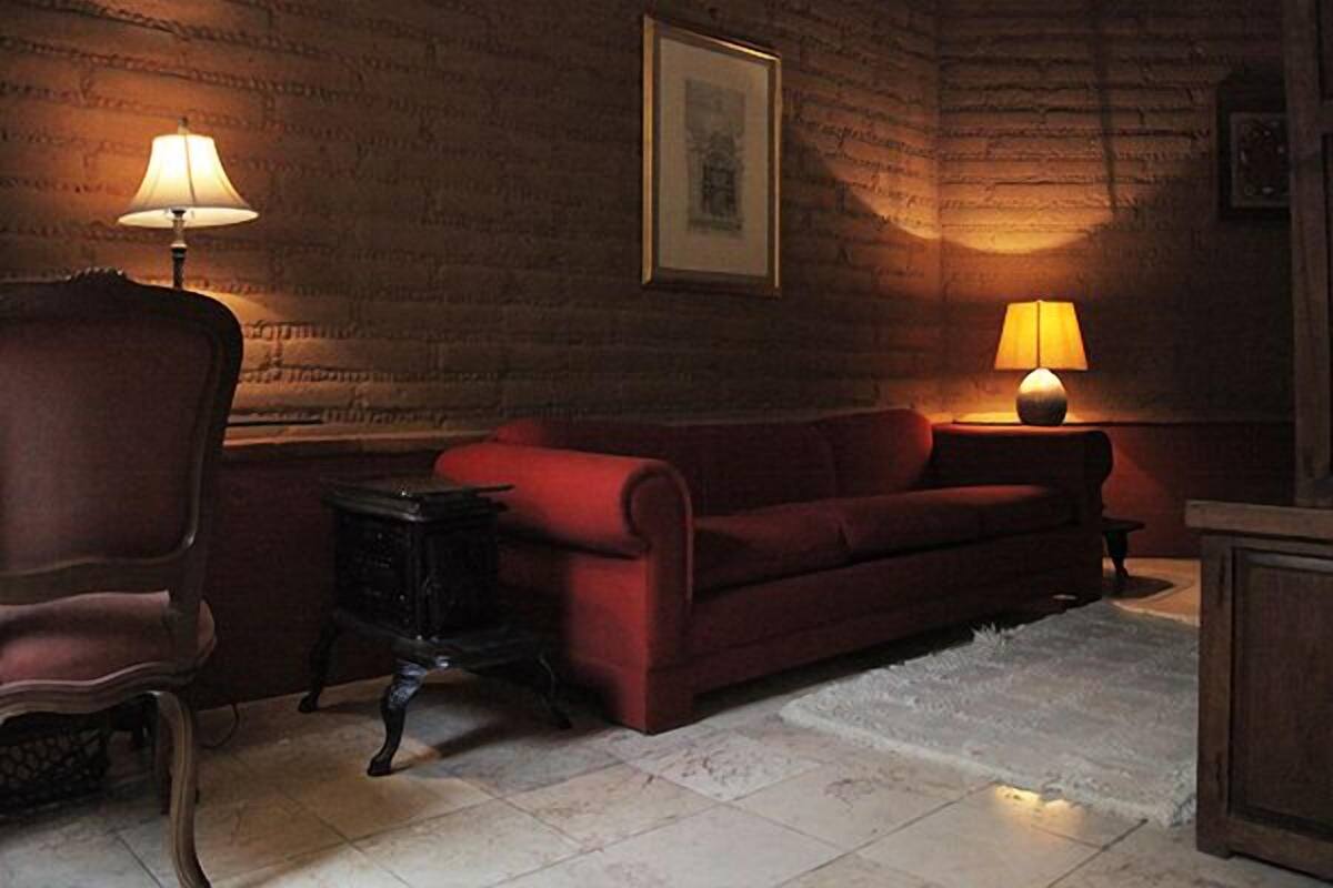 Une pièce avec un canapé rouge, deux lampes, un tableau encadré au mur et un tapis à motifs.