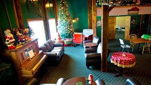 A cozy lobby with a piano, leather sofas, a Christmas tree, and a dining area with a red tablecloth. - Santas Lodge and Resort (Santa Claus)