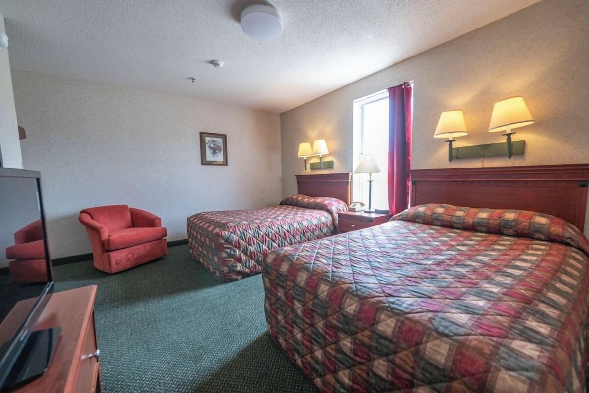 A hotel room with two beds, a TV, a red armchair, and two bedside lamps.