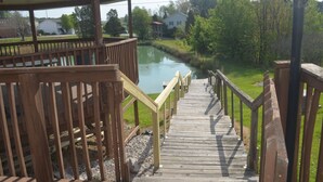 A wooden deck leading to a river with a gazebo and a house in the background. - Santas Lodge and Resort (Santa Claus)