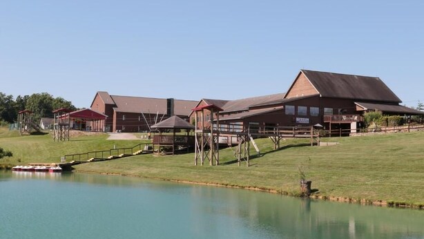 A large building with multiple sections, a covered walkway, and a body of water in the foreground. - Santas Lodge and Resort (Santa Claus)