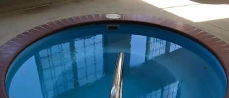 A circular indoor pool with a metal handrail, surrounded by a brick edge.