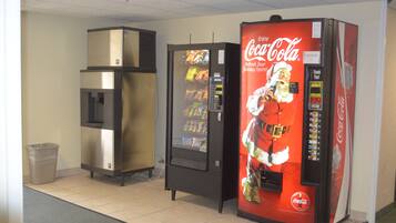 Uma área com máquinas de venda automática, incluindo uma máquina de Coca-Cola e um refrigerador.