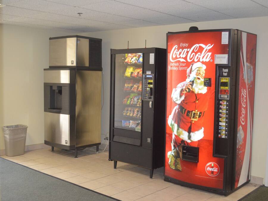 Uma área com máquinas de venda automática, incluindo uma máquina de Coca-Cola e um refrigerador.