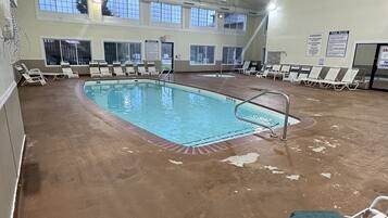 Una piscina interior con varias pistas de natación, rodeada de sillones de descanso y suelo de hormigón.