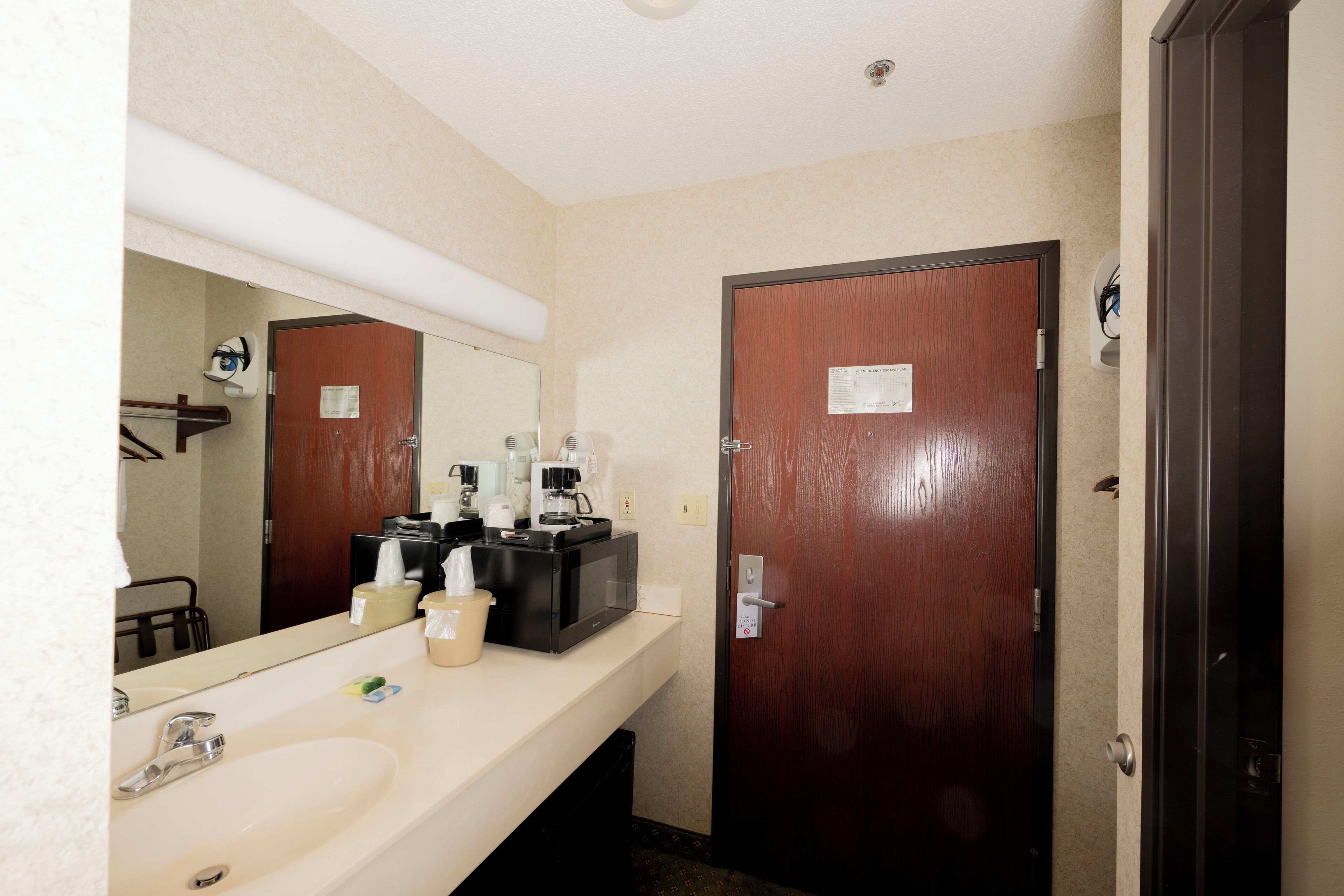 Une salle de bain d’hôtel avec un lavabo, un miroir et une porte sur laquelle est apposée une pancarte.