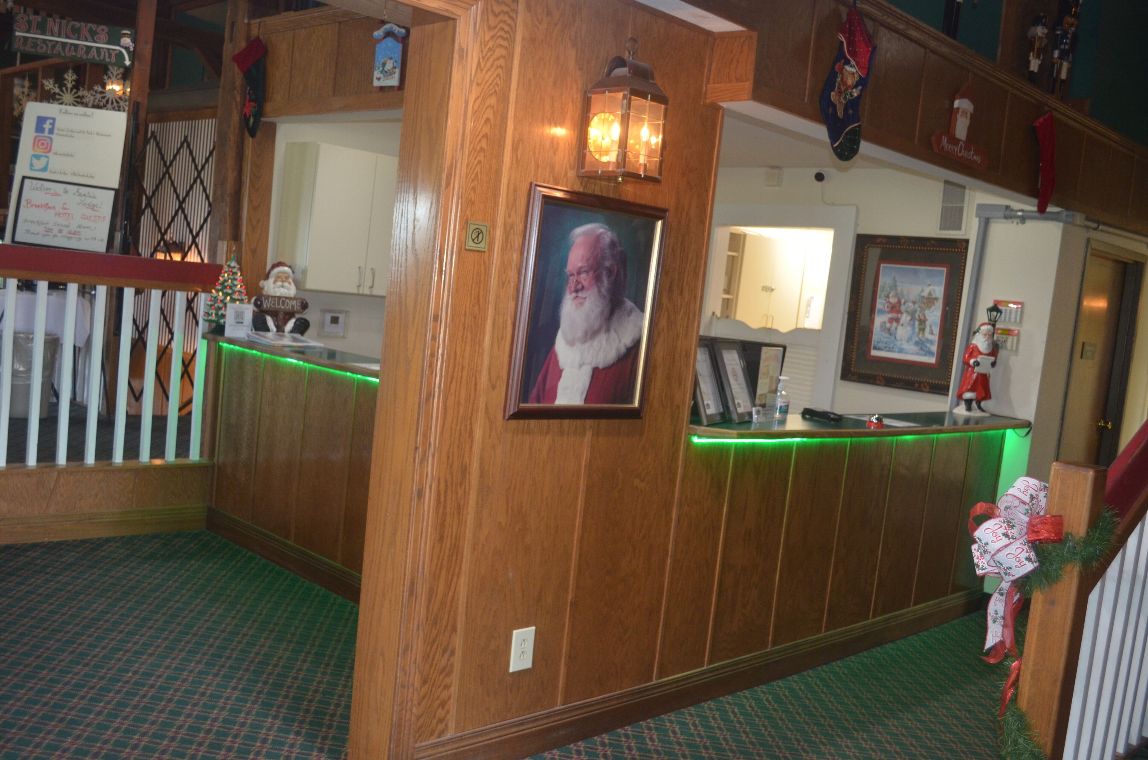 A wooden reception desk with a framed picture of Santa Claus, a green-lit counter, and a Christmas-themed wall decoration.