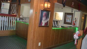 A wooden reception desk with a framed picture of Santa Claus, a green-lit counter, and a Christmas-themed wall decoration.