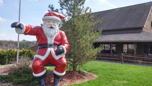 A large Santa Claus statue in front of a building with a sloped roof and wooden fence. - Santas Lodge and Resort (Santa Claus)