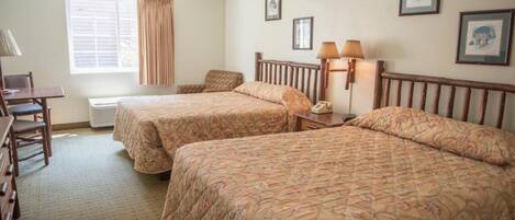 A hotel room with two beds, a desk, a chair, a lamp, and a window with curtains.