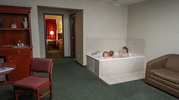 Relax in a spacious room with a large bathtub, comfortable sofa, and a wooden chair.