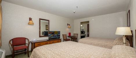 Quarto de hotel com duas camas, uma mesa com televisão, uma cadeira e um abajur.