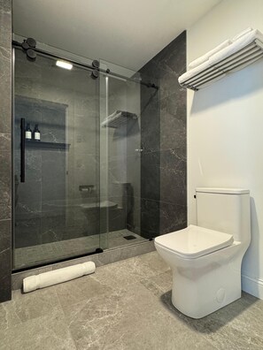 A modern bathroom with a glass-enclosed shower, a white toilet, and a towel rack.