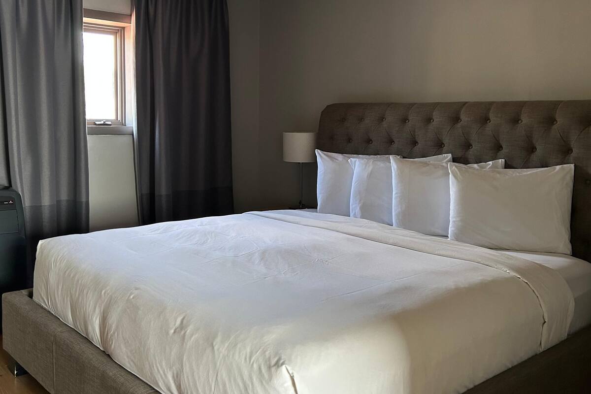 A neatly made bed with a grey upholstered headboard and white linens.