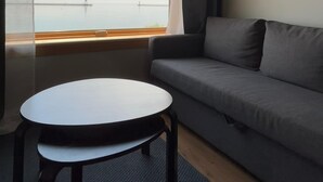 A room with a grey sofa, a small round table, and a window with a view of a bridge and the sky.