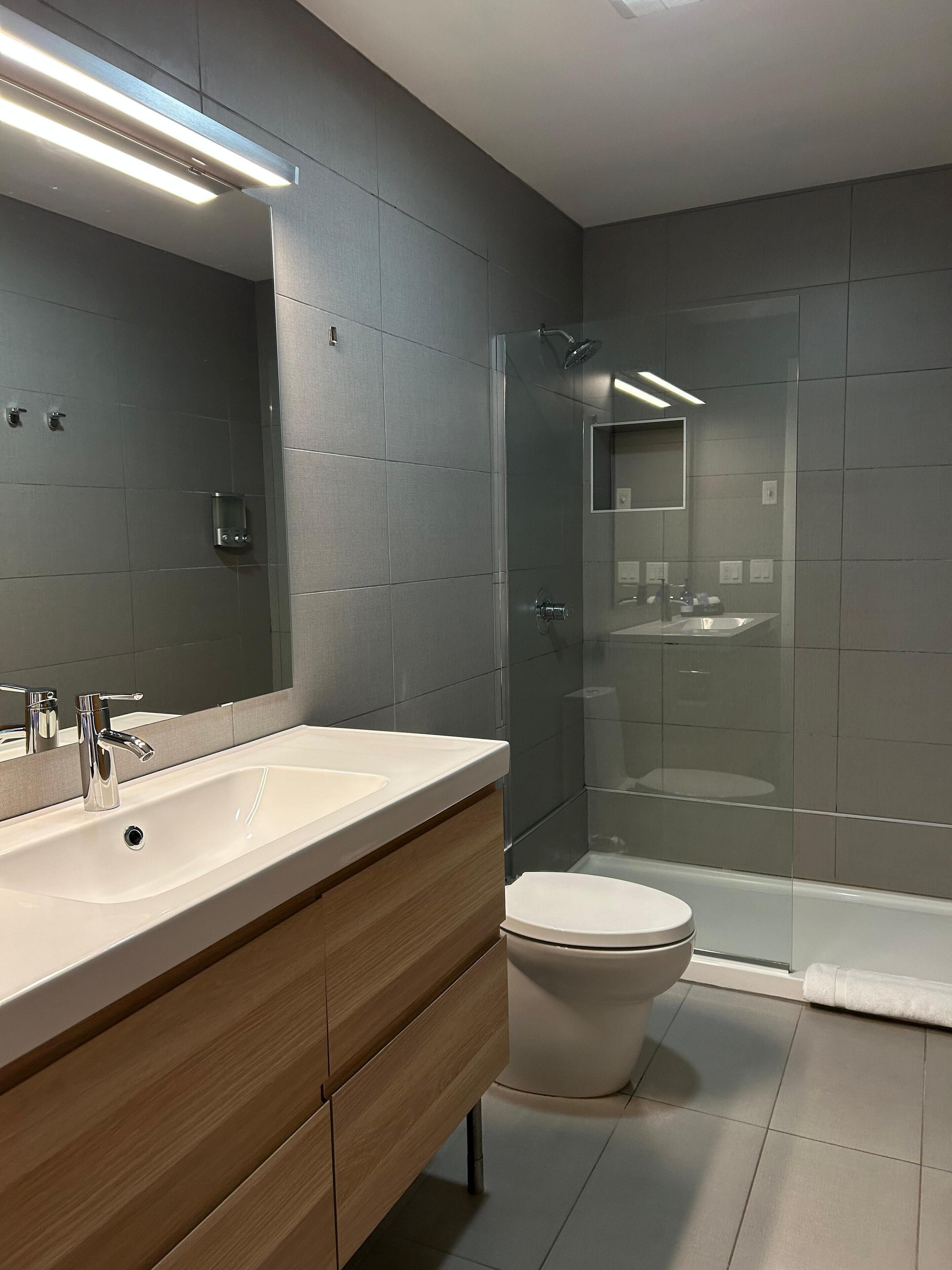 Une salle de bain moderne avec un grand miroir, deux lavabos, des toilettes et une douche à parois de verre.