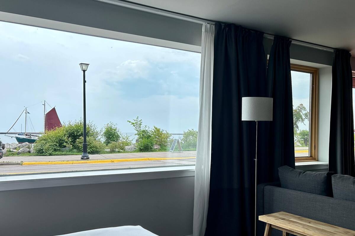A hotel room with a bed, a sofa, a lamp, and a view of a bridge and greenery.