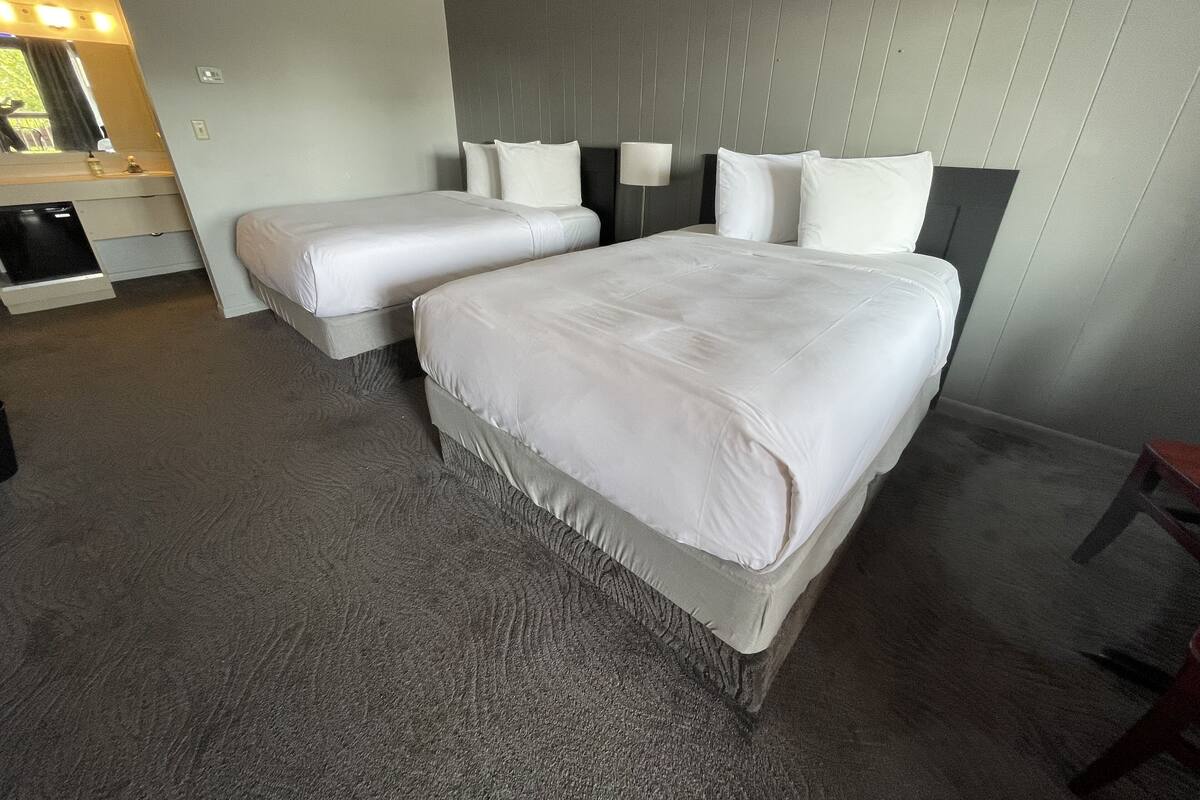 A hotel room with two beds, a small desk, a mirror, and a wall-mounted lamp.
