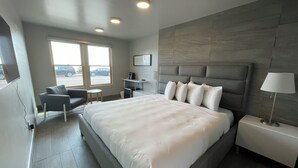 A modern hotel room with a large bed, a desk, a chair, and a view of the street through the window.