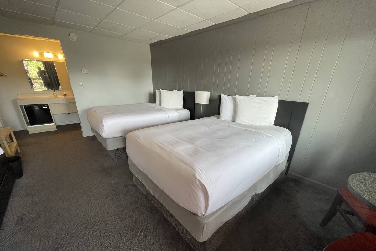 A hotel room with two beds, a small desk, a chair, and a mirror.