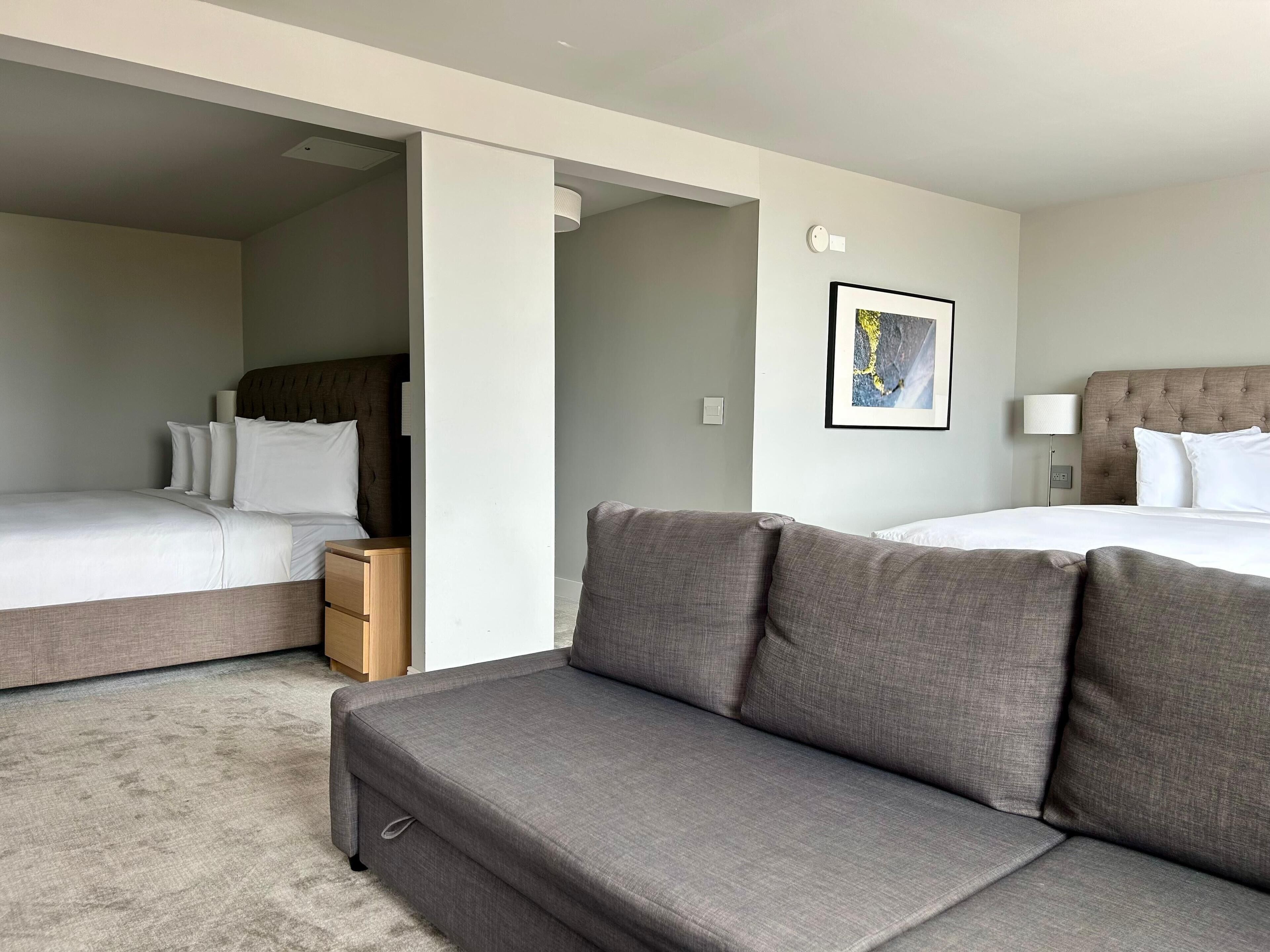A hotel room with a bed, a sofa, a nightstand, and a framed picture on the wall.