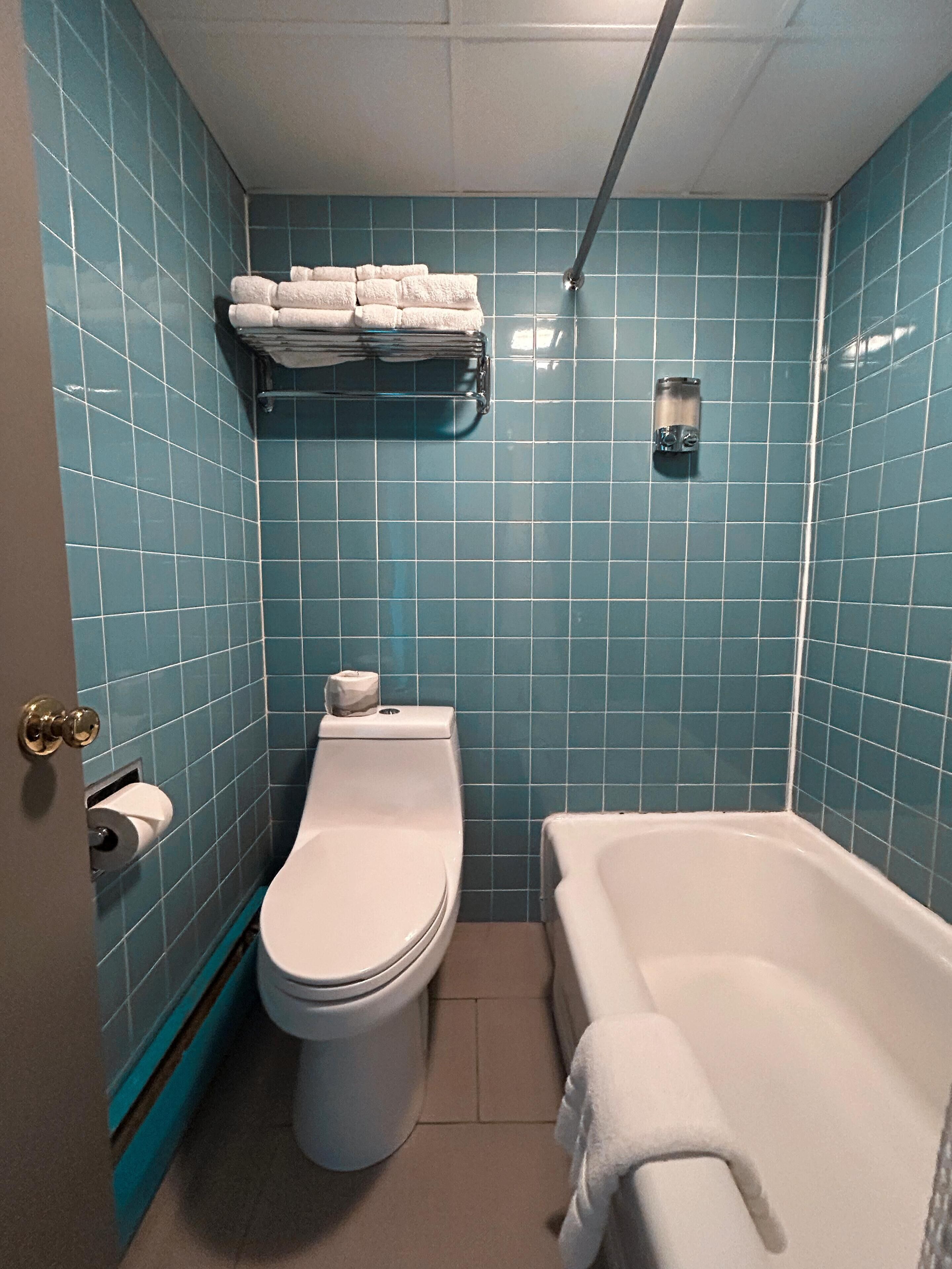 A bathroom with blue tiles, a toilet, a bathtub, and a towel rack.