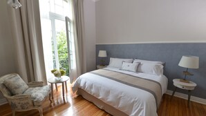 Un dormitorio con una cama grande, dos mesitas de noche, una silla y una ventana con cortinas.