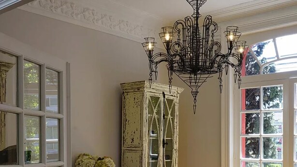 Un comedor con una mesa de madera, sillas de mimbre, una araña y un mueble alto blanco con puertas de cristal.