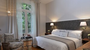 Un dormitorio con una cama grande, dos lámparas de noche, una silla y una mesita con un jarrón de flores.