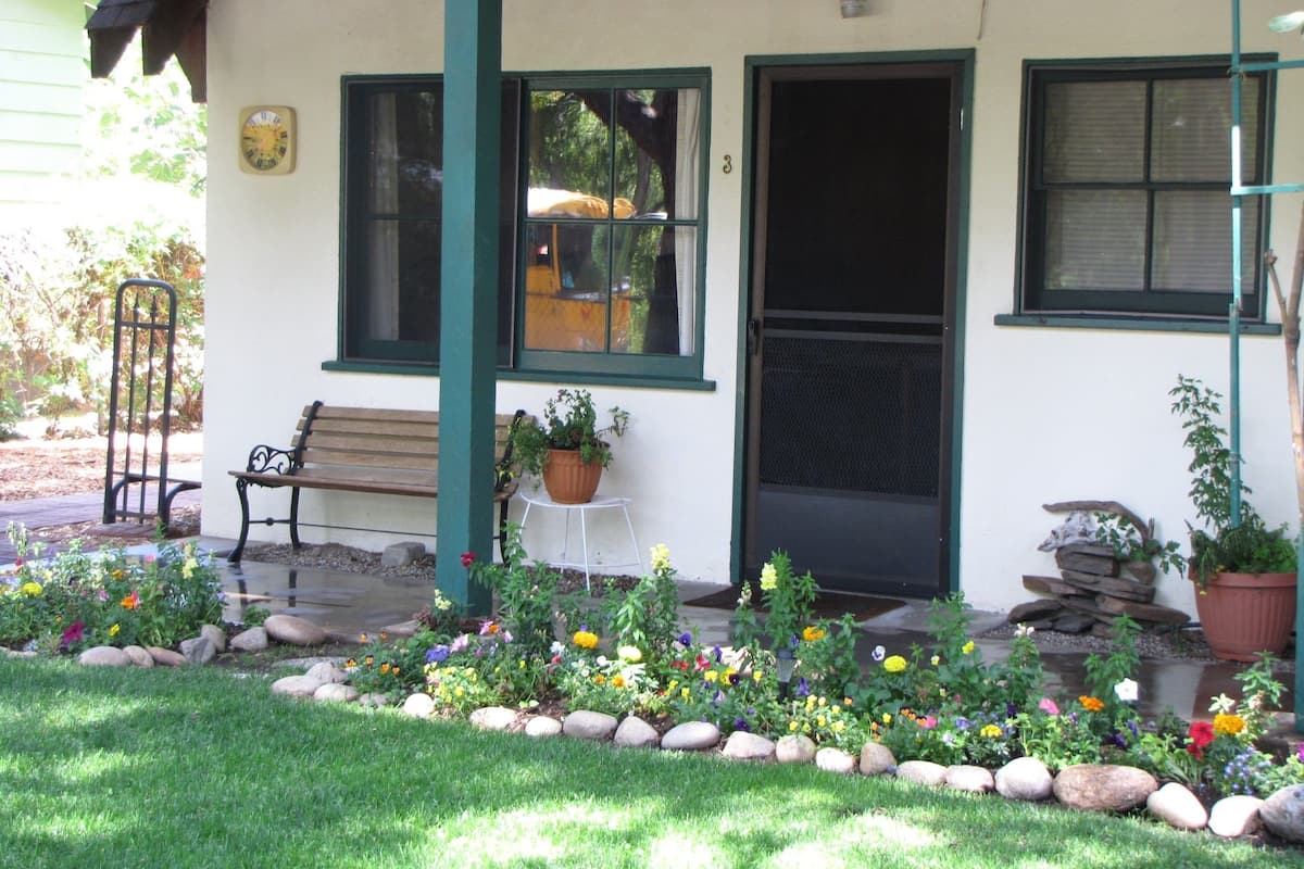 A building with a porch, a bench, a potted plant, and a flower bed.