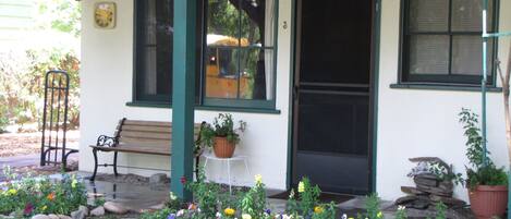 A building with a porch, a bench, a potted plant, and a flower bed.