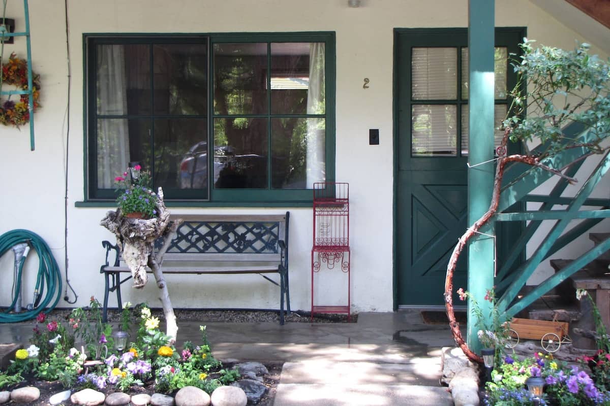 A house with a green door, a bench, and a garden with flowers and rocks.
