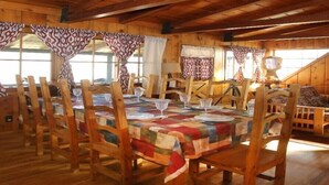 A wooden dining room with a table set for six, wooden chairs, and curtains. - Kern Riverfront Lodge (Kernville)