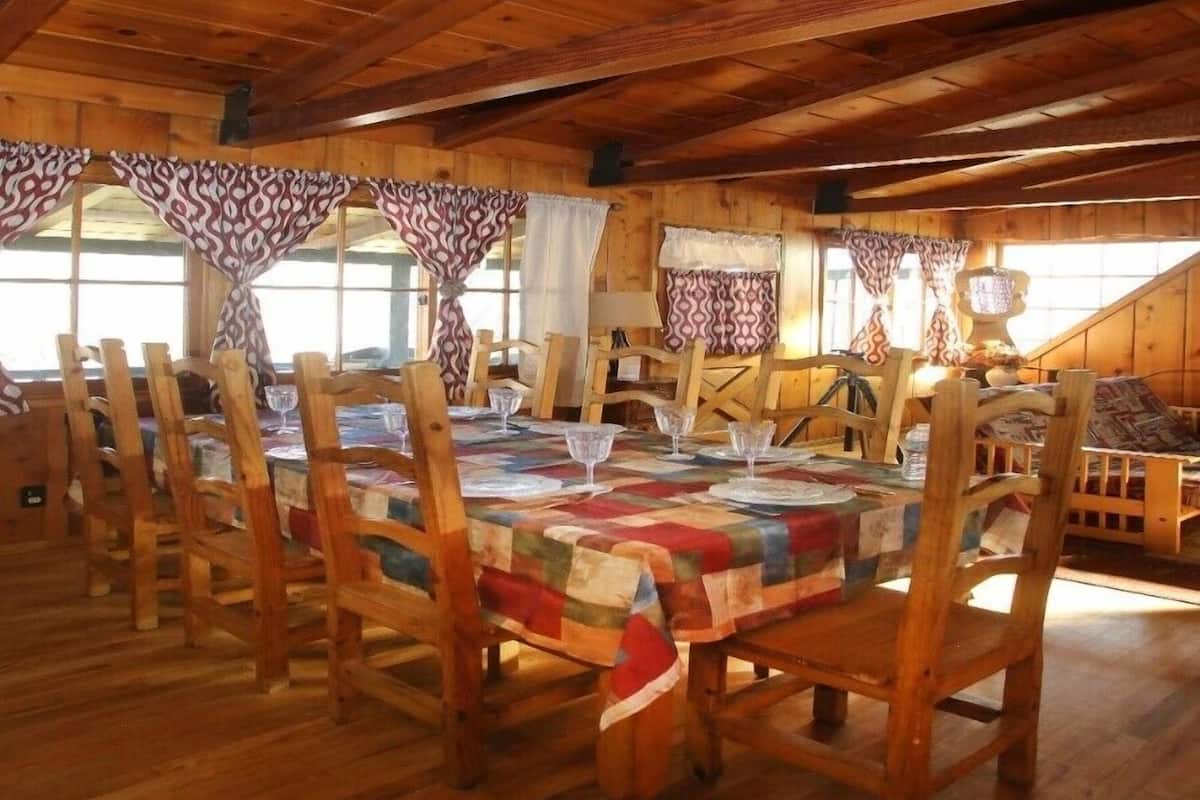 A wooden dining room with a table set for six, wooden chairs, and curtains.