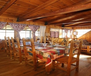 A wooden dining room with a table set for six, wooden chairs, and curtains. - Kern Riverfront Lodge (Kernville)