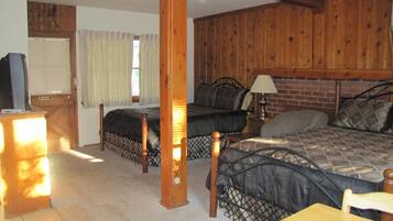 A room with two beds, a wooden table, a TV, and a window with curtains.