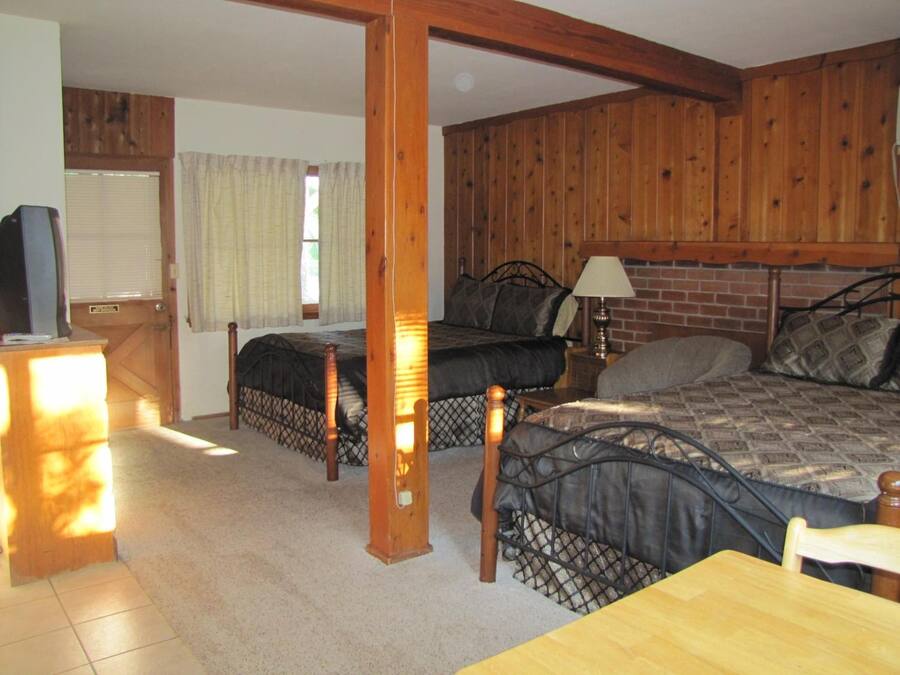A room with two beds, a wooden table, a TV, and a window with curtains.
