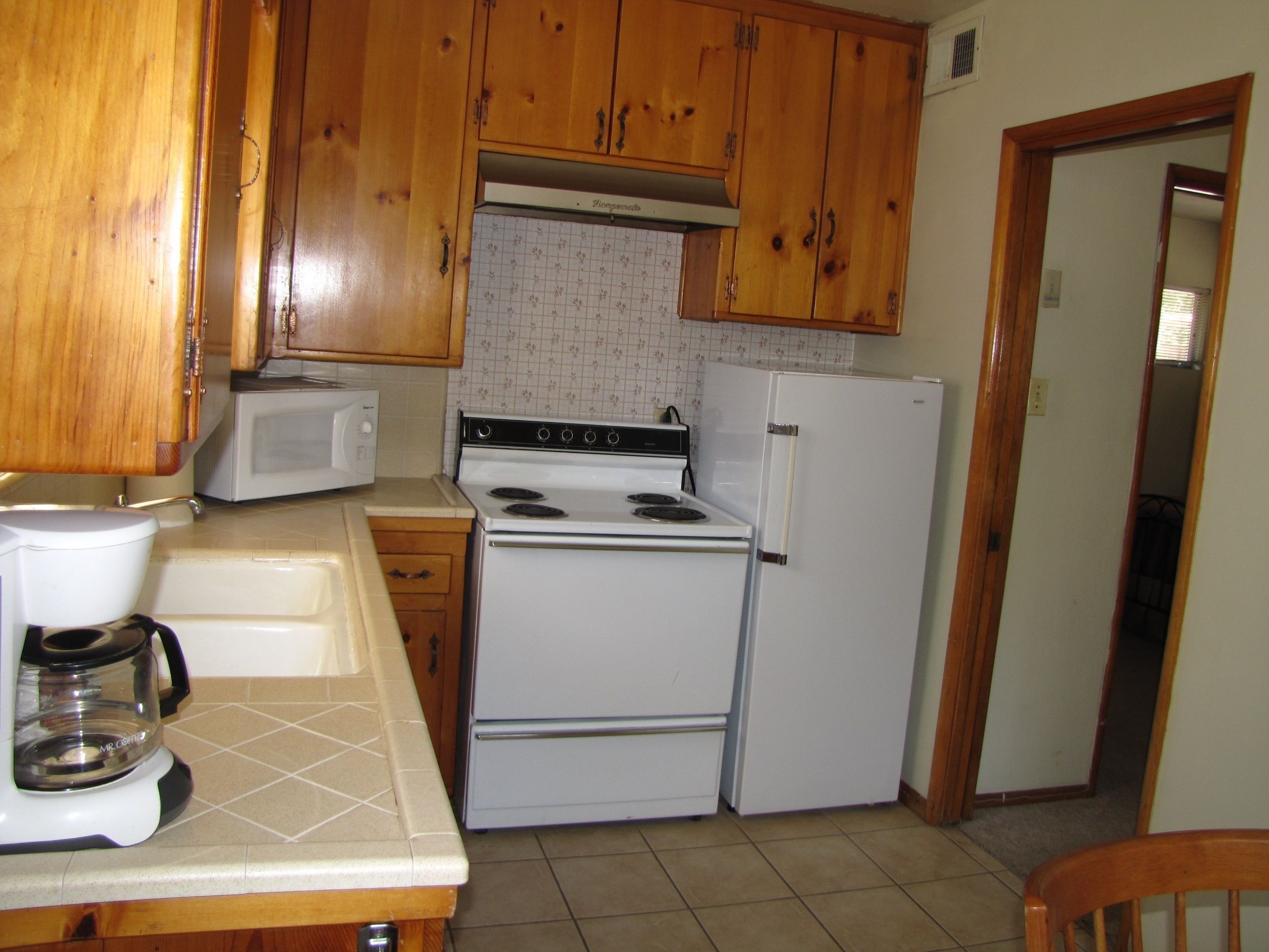 A kitchen with wooden cabinets, a white stove, a white refrigerator, and a microwave.